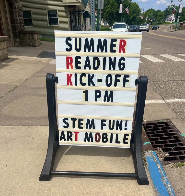 Sandwich board sign on the sidewalk announcing library summer reading program.